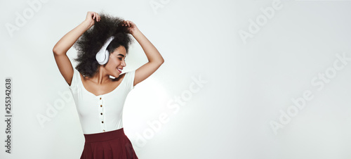 Listening her favorite song. Charming afro american woman listening to music and keeping eyes closed while standing against grey background. Space for text. Web Banner