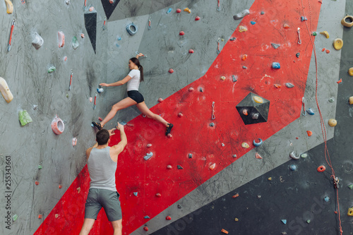 Attractive woman climber determined to overcome the height. Young man instructor pointing how to move.copy space. walking on the wall