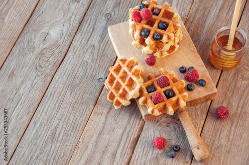 Traditional waffles with fresh raspberries and blueberries on lace doily on wooden background. 