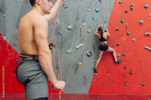 young handsome man having a rest at gym while the active girl enjoying climbing. free time activity