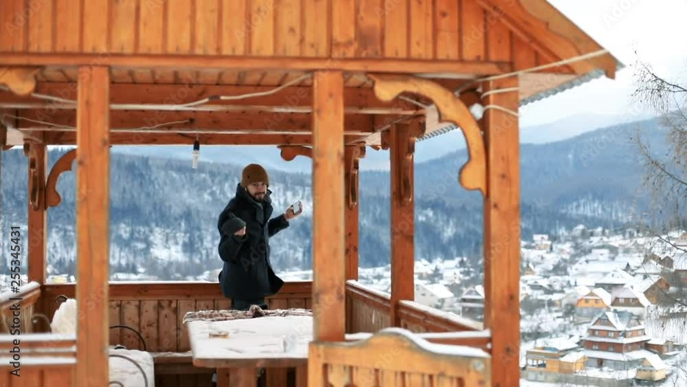 Happy man smiling and gesturing using his smartphone in small arbor over majestic snowy mountains in the countryside. Happy man smiling and gesturing using his smartphone in small arbor over majestic snowy mountains in the countryside.