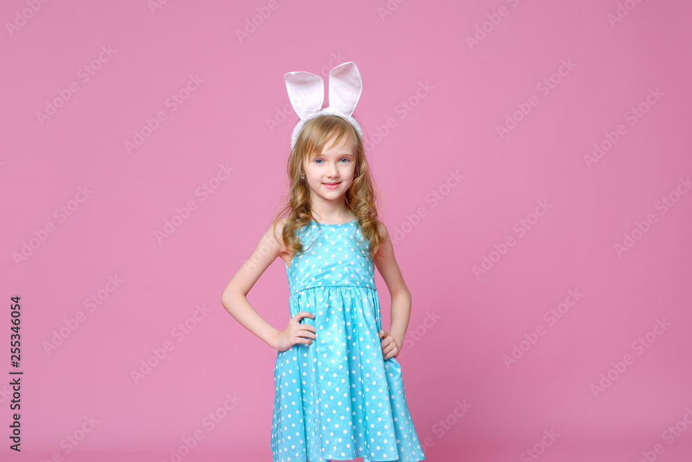 Cute little blonde girl in the shape of an Easter Bunny and a blue dress with a pea pattern holds her fingers . Concept of the celebration, advertising and fashion. happy Easter. Selective focus.