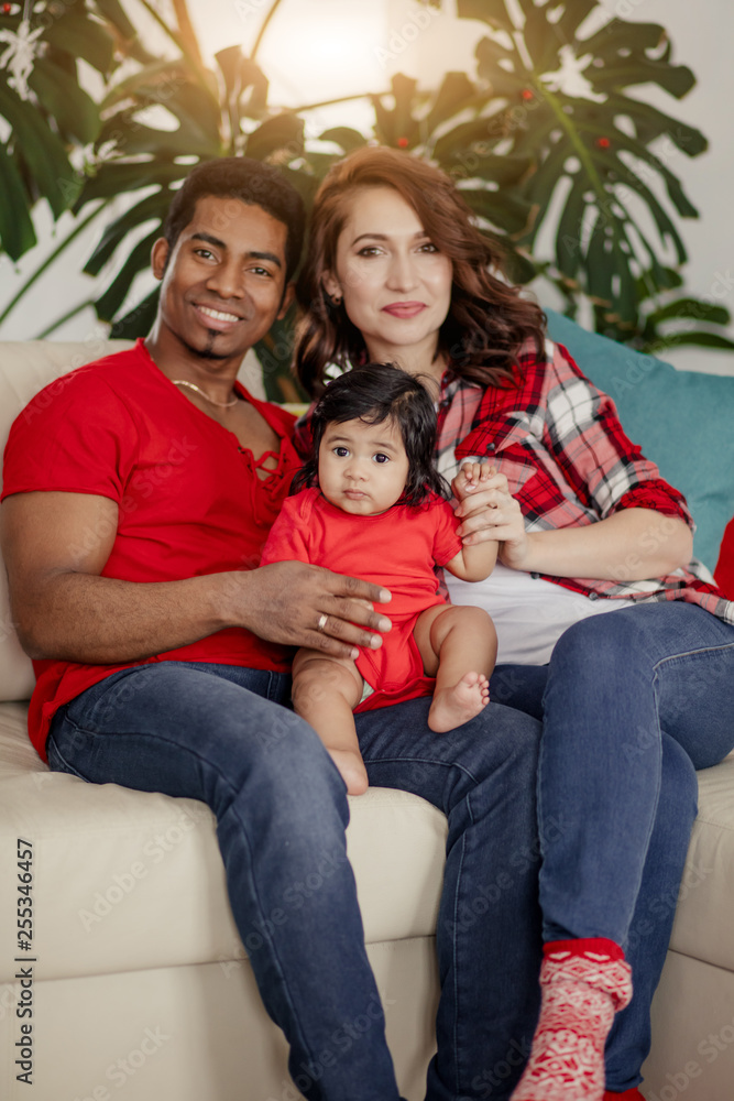 Happy parents and baby girl sitting on the couth and posing to the camera, close up photo.love, closeness Happy parents and baby girl sitting on the couth and posing to the camera, close up photo.love, closeness