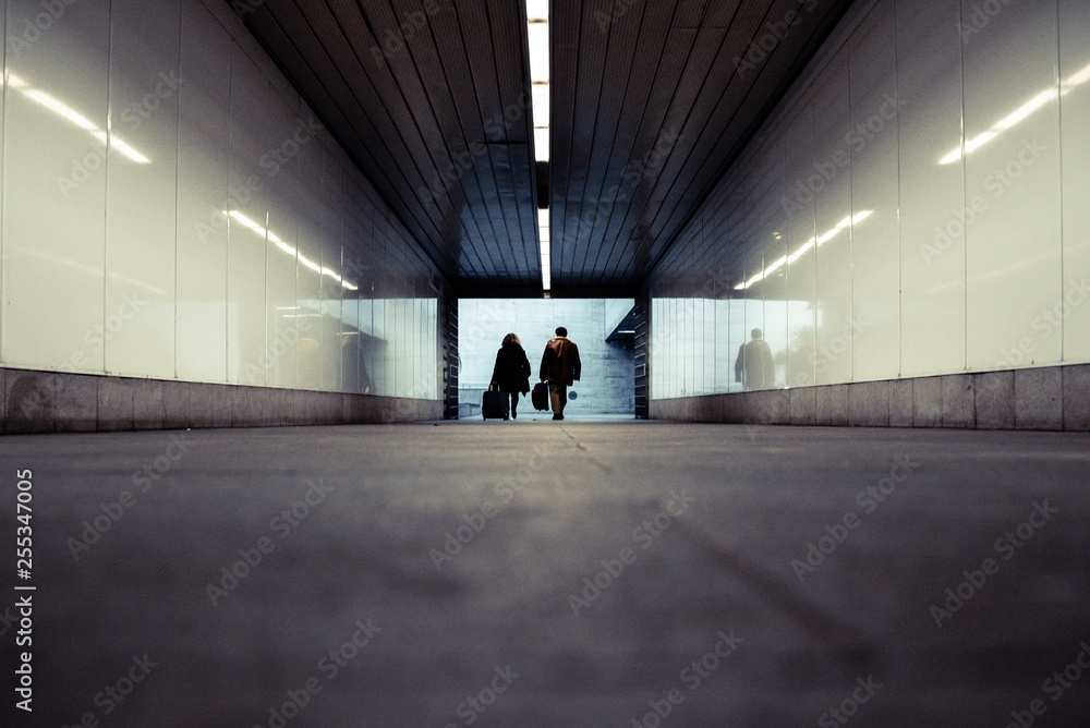 People walking through an underground subway corridor with suitcases trolley.