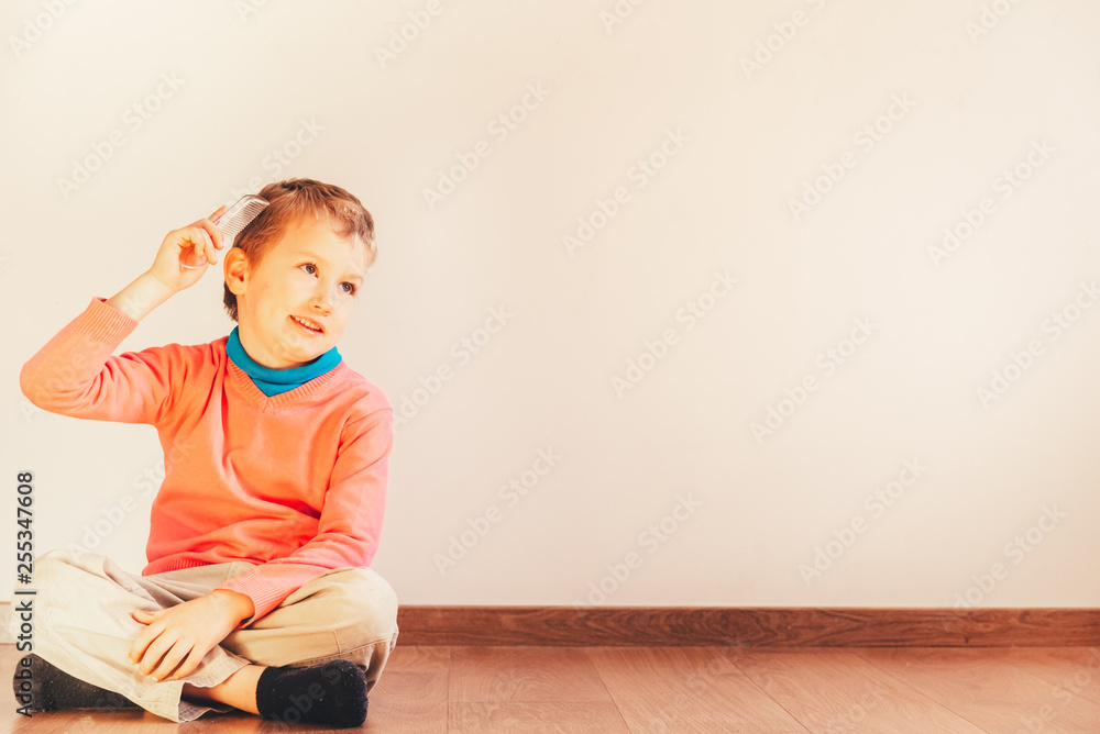Child sitting on the floor of his house looking handsome while he only combs his hair, concept of independent and autonomous child. - obrazy, fototapety, plakaty 