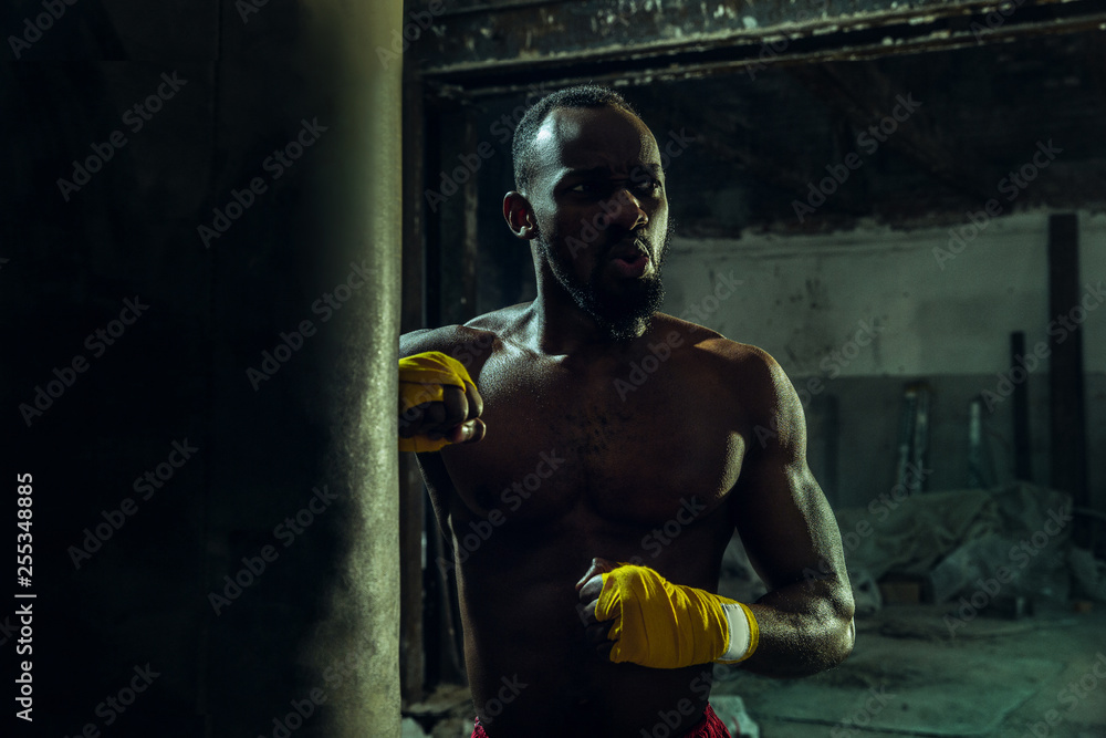 Hands of boxer over dark gym background. Strength, attack and motion concept. Fit african american model in movement. Naked muscular athlete. Sporty man during boxing.