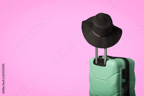 Plastic suitcase on wheels and a hat with a wide brim on the handle on a pink background. Travel concept, vacation trip, visit to relatives photo