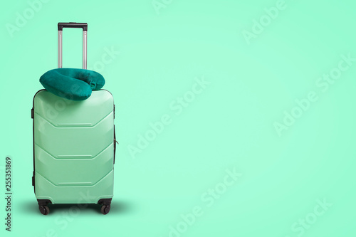 Plastic suitcase and travel pillow on a green background. Concept of travel, business trips, trips to visit friends and relatives