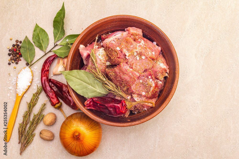 Raw pork shoulder. Spices, dry herbs, garlic, rosemary, bay leaf, hot pepper and mix, nutmeg, onion, salt. Ingredients for marinating meat in rustic ceramic bowl on stone background top view close up