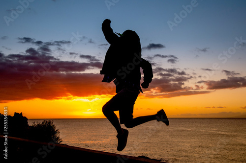 Silhouette of young boy jumping near the sea at the sunset Concept image of freedom and happiness of a teenager Teen jump with ocean and sunlight in background Postcard from a summer holiday vacation