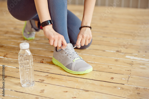 Close-up front view of woman's hands tying shoelaces on sneakers in the gym