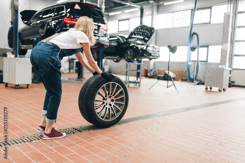 pleasant female mechanic changing a wheel at the garage. full length photo. side view photo.job. occupation. copy space