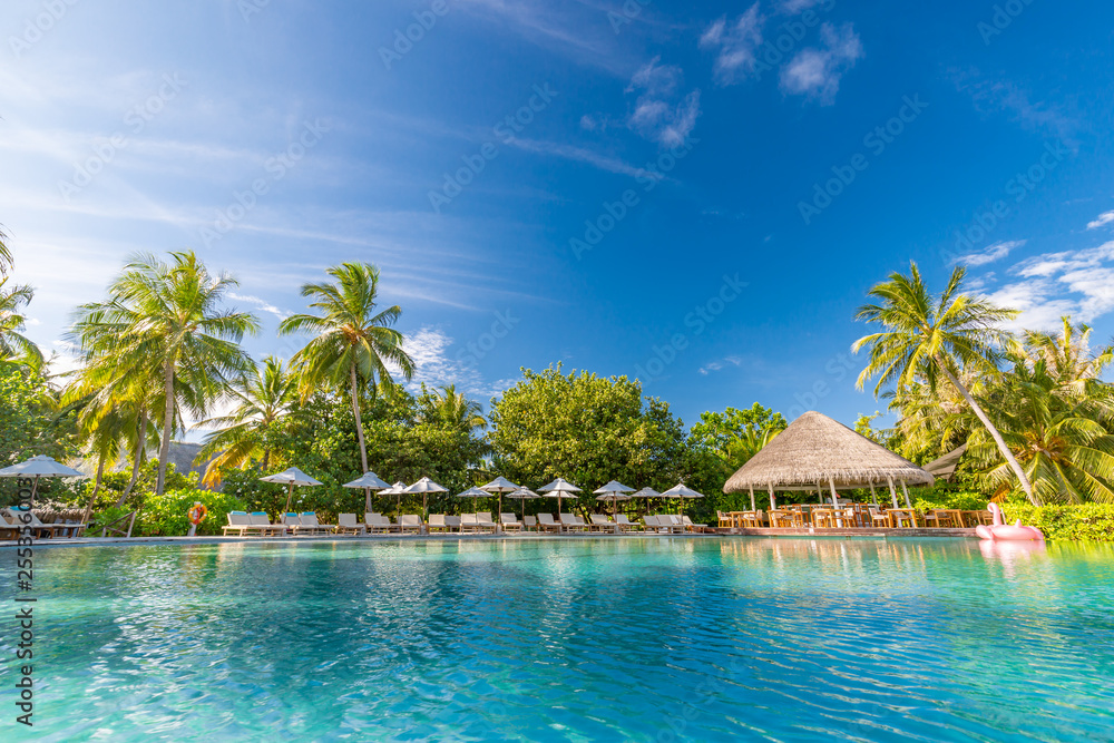 Luxurious poolside with loungers and umbrellas under palm trees and blue sky. Perfect summer beach vacation and holiday, tropical beach resort concept