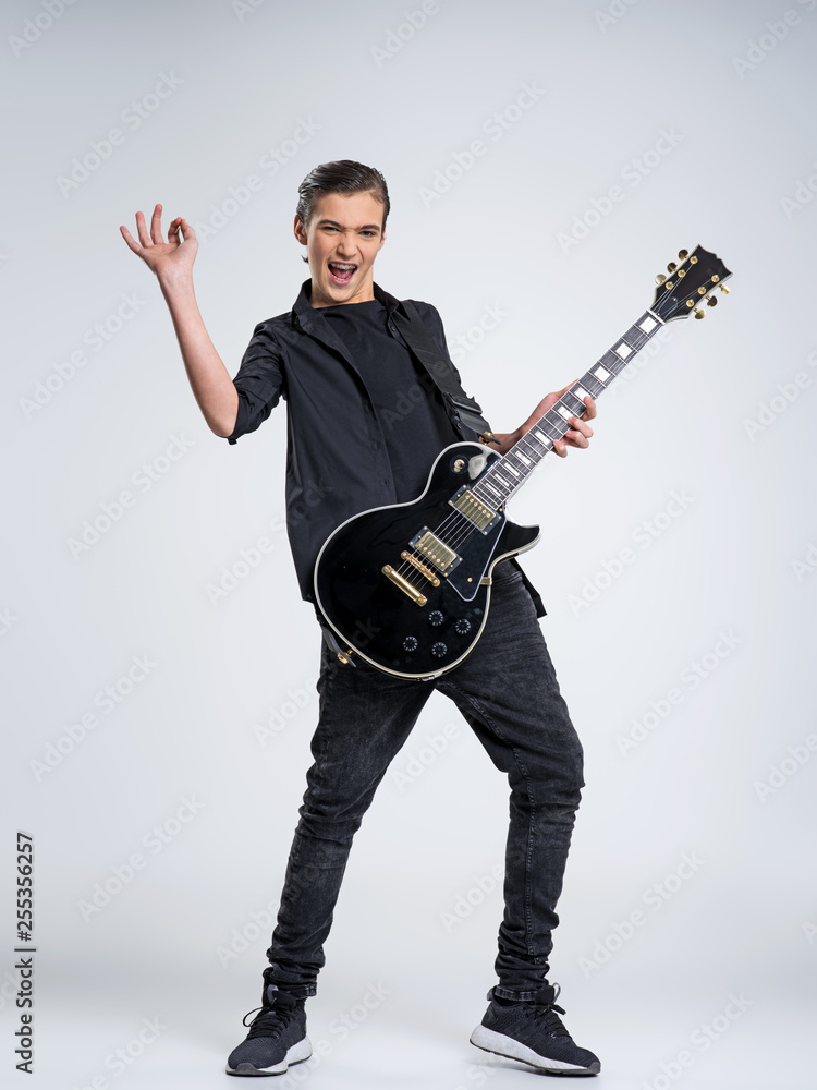 Fototapeta premium Fifteen years old guitarist with a black electric guitar. Teenage musician holds guitar