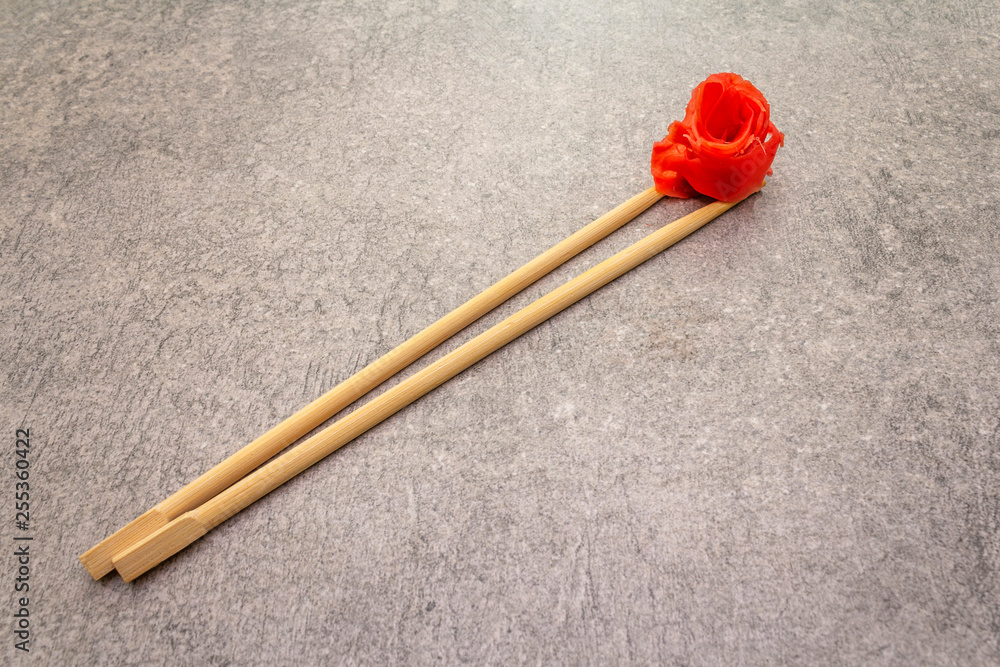 Pickled sushi ginger slices in chopsticks on stone background, top view Pickled sushi ginger slices in chopsticks on stone background, top view