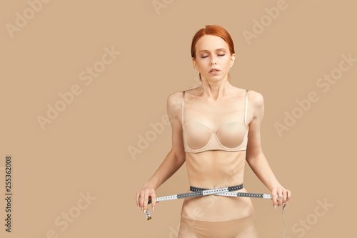 beautiful fashion top model measures her waist with meter on beige background. Healthcare and beauty concept. Double standards. Anorexia as a norm for fashion industry