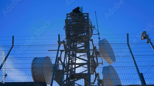Weather radar with a rotating radiodetection antenna on top of a mountain collects weather data from whole around area against flares in the camera lens. Shot in motion