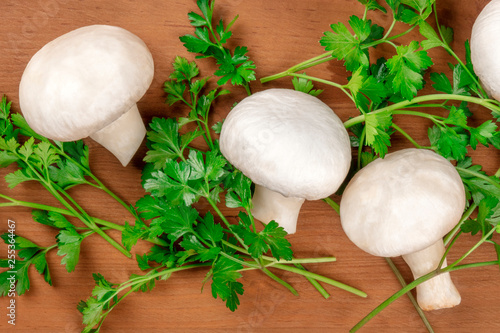Champignon mushrooms, shot from the top on a rustic wooden background with fresh parsley leaves