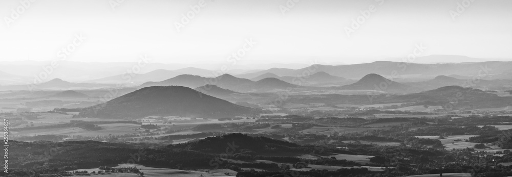 Silhouettes of volcanic hills of Ceske Stredohori, Central Bohemian Uplands, on sunny and hazy day. Czech Republic