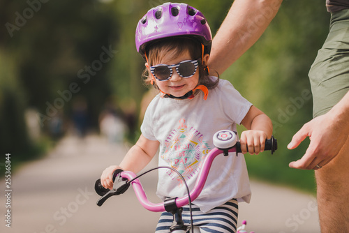 Fototapeta Naklejka Na Ścianę i Meble -  father teaches little toddler daughter to ride a bike in the park