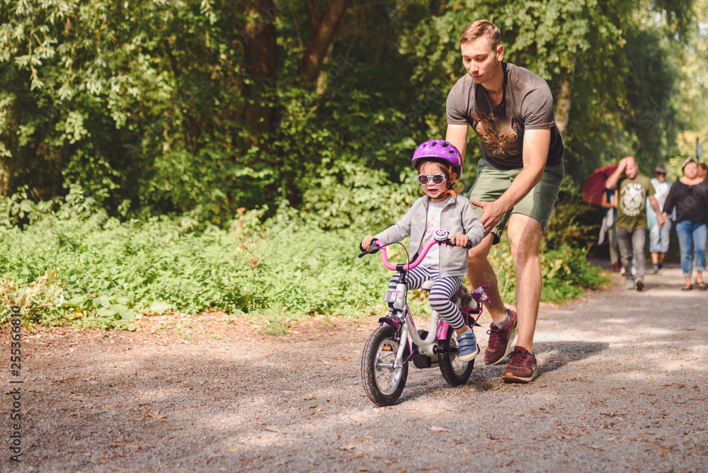 father teaches little toddler daughter to ride a bike in the park father teaches little toddler daughter to ride a bike in the park