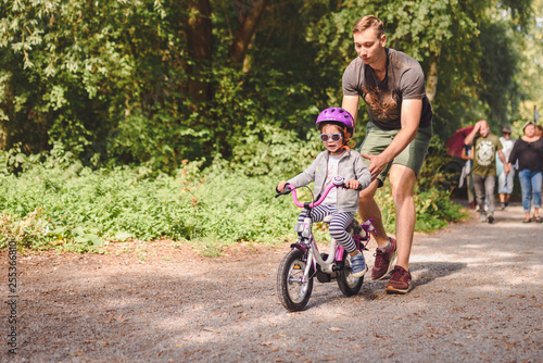 father teaches little toddler daughter to ride a bike in the park © very_ulissa
