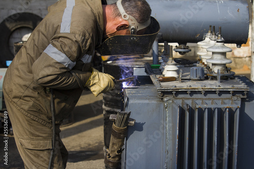 welder repairing an electrical transformer. electrical equipment breakdown and repair work on the restoration of electricity concept