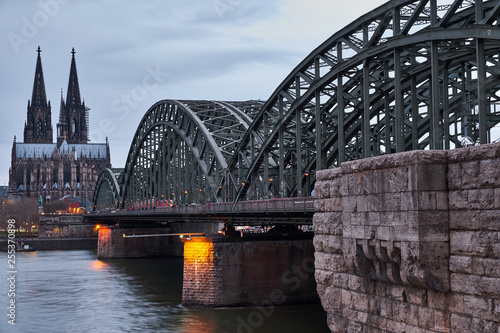 Der berühmte Blick auf die Wahrzeichen von Köln bei Tag. Über die Hohenzollernbrücke fahren täglich hunderte Züge und tausende Menschen, während sie den Ausblick auf das Kölner Panorama genießen. © 77pixels