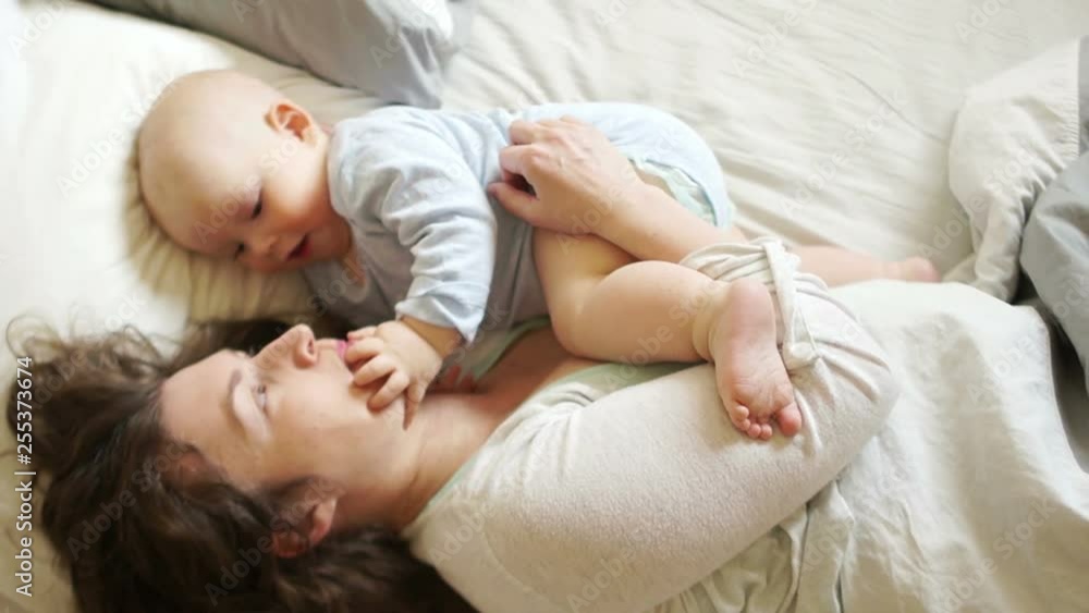 Mature mother plays with the baby lying in bed. The kid touches his finger to the mouth of the mother, the development of kids Mature mother plays with the baby lying in bed. The kid touches his finger to the mouth of the mother, the development of kids