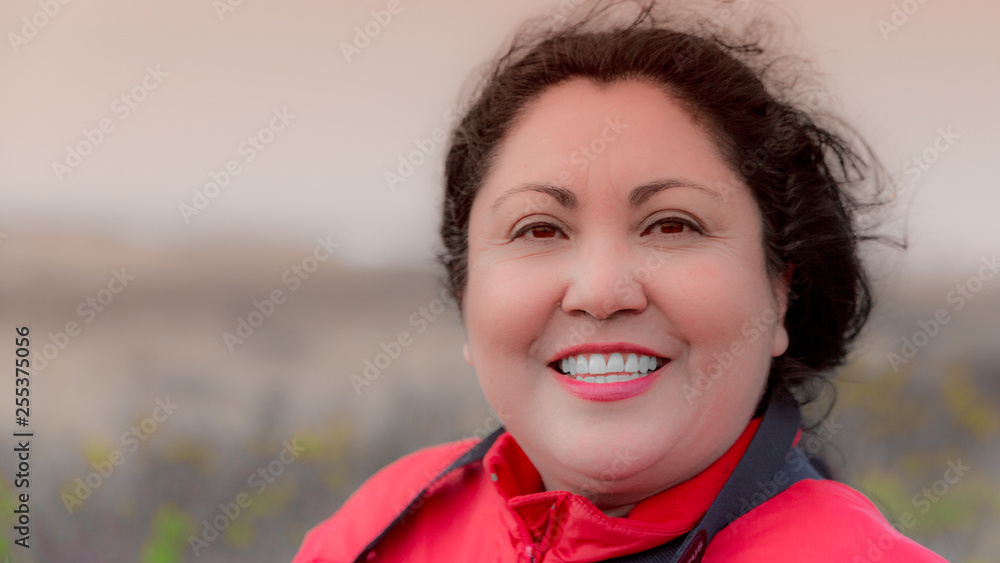 Beautiful happy smiling latin woman on a wonderful windy day with a blurry brown background with little green touches