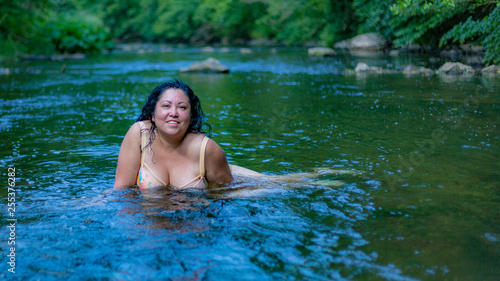Beautiful latin woman with long black hair enjoying a wonderful summer day in the Ahr river in Schuld Germany with green vegetation on a blurred background © Emile