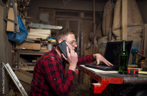 Young carpenter in workshop using phone and laptop