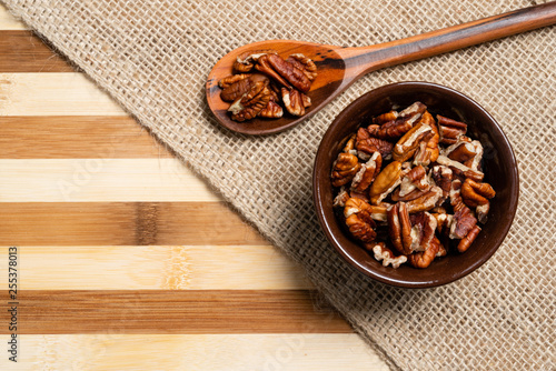 Peeled pecan nuts inside brown pottery and wooden spoon on bamboo wood background. photo