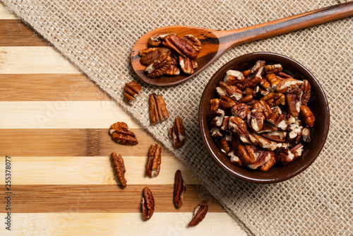 Peeled pecan nuts inside brown pottery and wooden spoon on bamboo wood background. photo