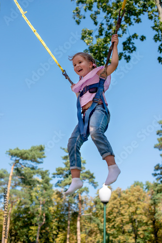 Emotional portrait of the girl with seat belts on an attraction "Trampoline". She with delight soars in air against the background of the blue sky