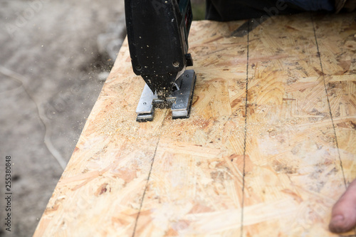 cutting an osb panel with a jigsaw, hand on the panel