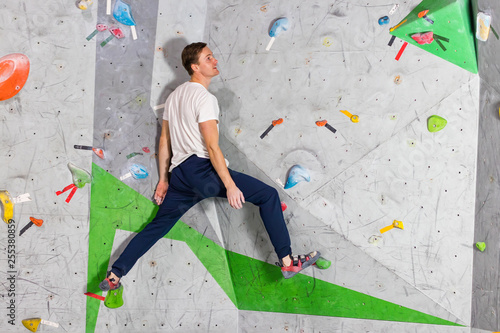 Rock climber man hanging on a bouldering climbing wall, inside on colored hooks