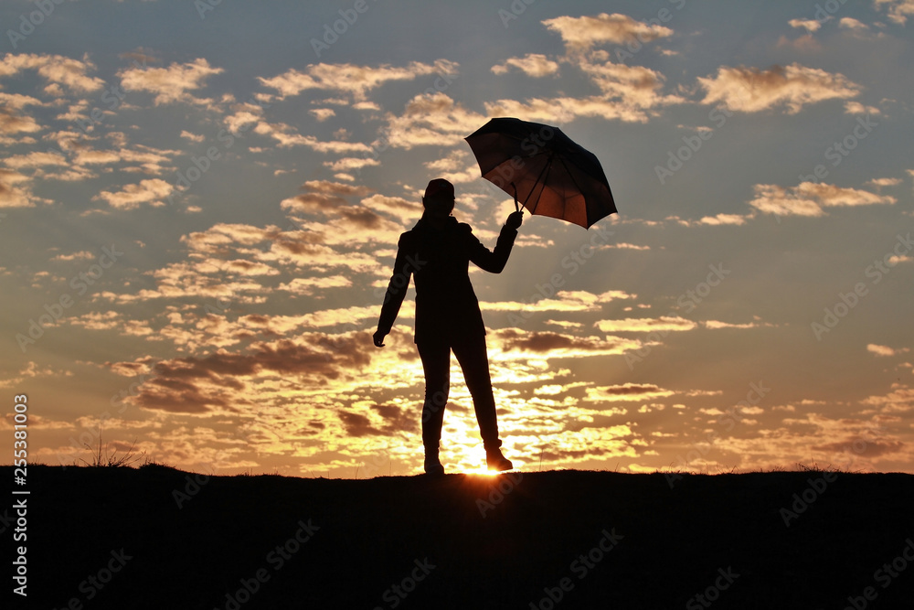 Silhouette girl with umbrella on the background of incredible sunset, sky and clouds