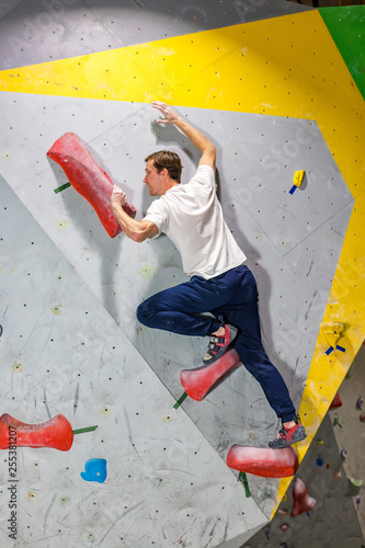 Rock climber man hanging on a bouldering climbing wall, inside on colored hooks