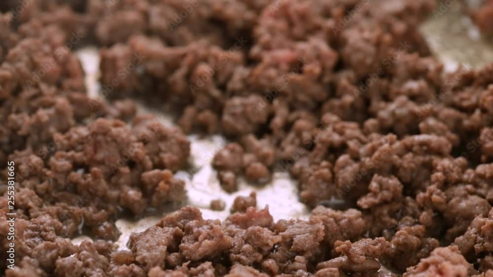 Close slow motion video of browned hamburger meat being stirred in a cooking pan with a wood spoon illuminated with natural lighting. Close slow motion video of browned hamburger meat being stirred in a cooking pan with a wood spoon illuminated with natural lighting.