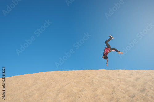 young asian male make an acrobatic backflip moves on a sand dune. concept of freedom, happiness, travel and active lifestyles