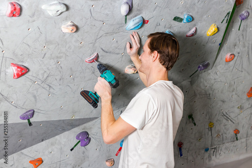 Rock climber fastens the hook with a screwdriver at the climbing wall in the boulder hall