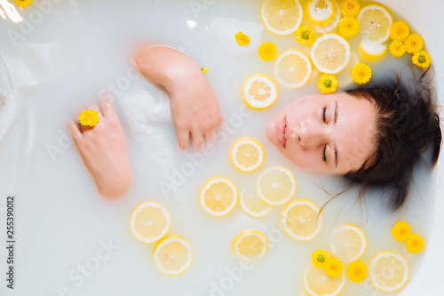 young woman in milk bath with lemons and yellow flowers relaxing spa. photo
