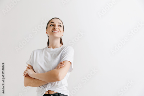 Happy woman standing and smiling isolated on gray studio background. Beautiful female half-length portrait. Young emotional woman. The human emotions, facial expression concept.