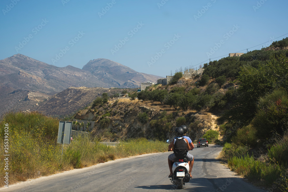 Travelers couple on scooter riding a mountain road. Crete island, Greece Travelers couple on scooter riding a mountain road. Crete island, Greece