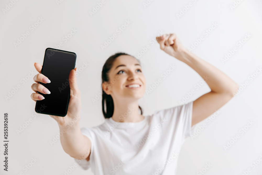 Portrait of a confident casual girl showing blank screen of mobile phone isolated over gray background at studio. Portrait of a confident casual girl showing blank screen of mobile phone isolated over gray background at studio.