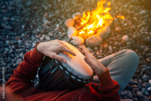 percussionist playing djembe sitting by fire, close-up photo