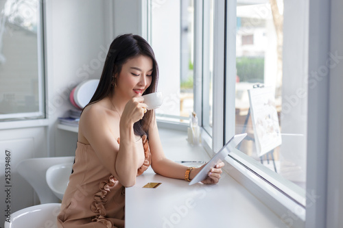 Young asian woman sitting drinking coffee and using tablet at coffee shop. Free Download Young asian woman sitting drinking coffee and using tablet at coffee shop. - GFXLoad