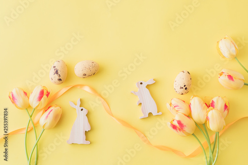 Flat lay spring composition with yellow tulips and easter eggs on a yellow background