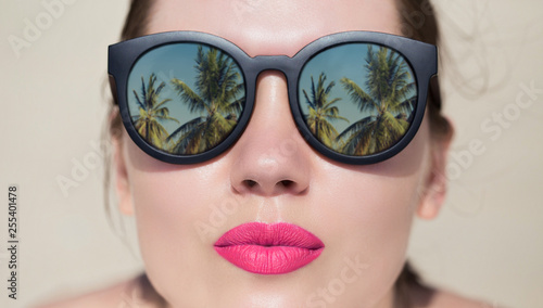 Portrait close up of a pretty woman with bright pink painted lips and reflection of palms in sunglasses